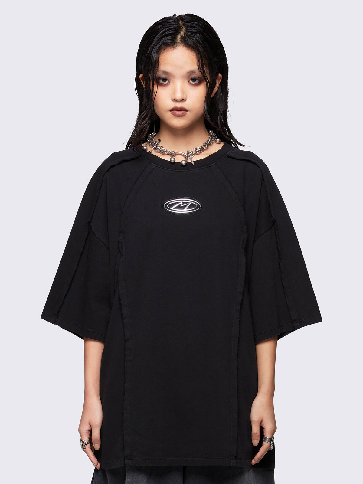 Black oversized t-shirt featuring exposed seams details and front metallic signature patch detail.
