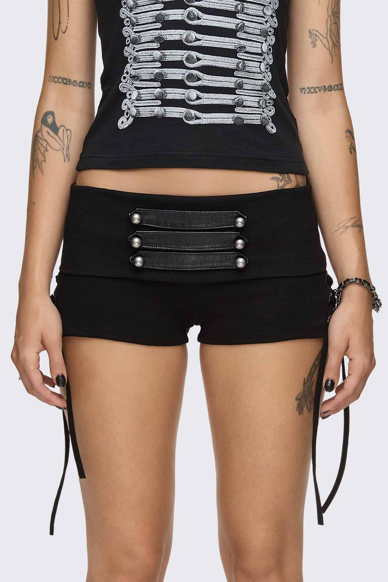 Black hot pants with lace-up sides, faux leather straps, silver dome buttons and a wide fold-over waistband.