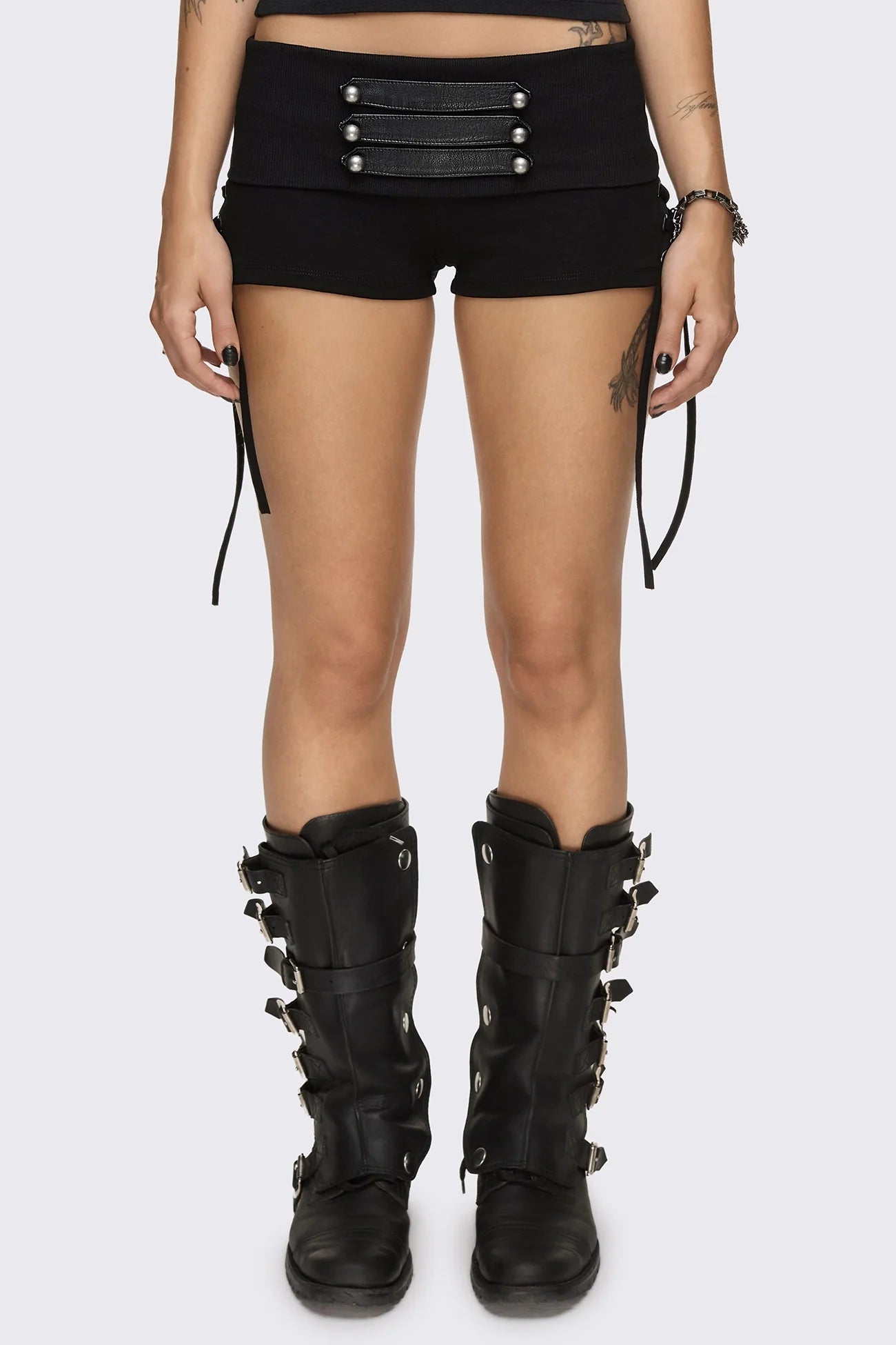 Black hot pants with lace-up sides, faux leather straps, silver dome buttons and a wide fold-over waistband.