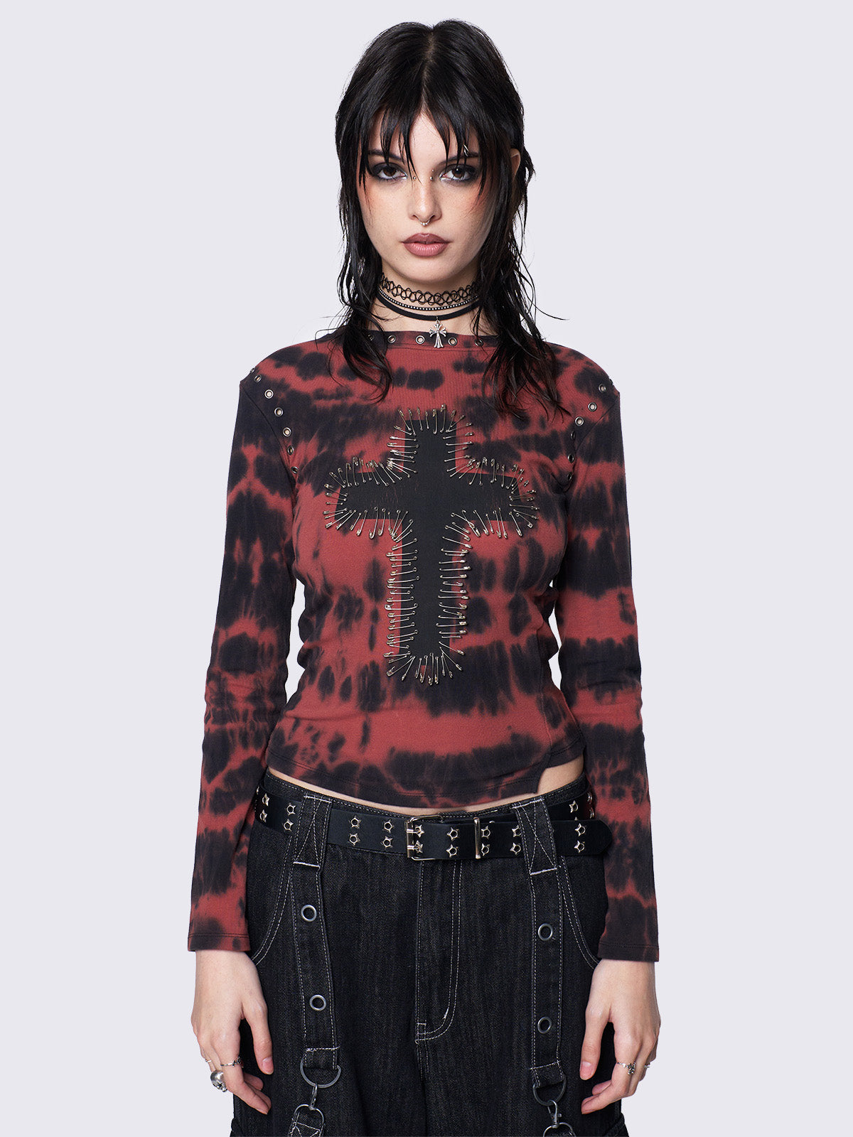 Asymmetric long sleeve top with black and red tie-dye pattern, cross patch with safety pins, silver eyelets at neckline and armhole, slim fit.