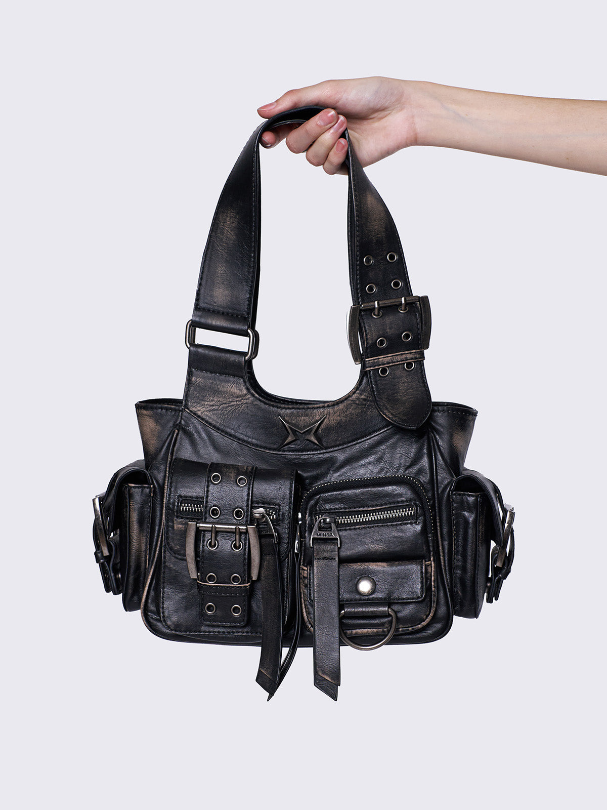 Black leather handbag with multiple pockets, buckles, and a star design, held by a hand, featuring an edgy, utilitarian style.
