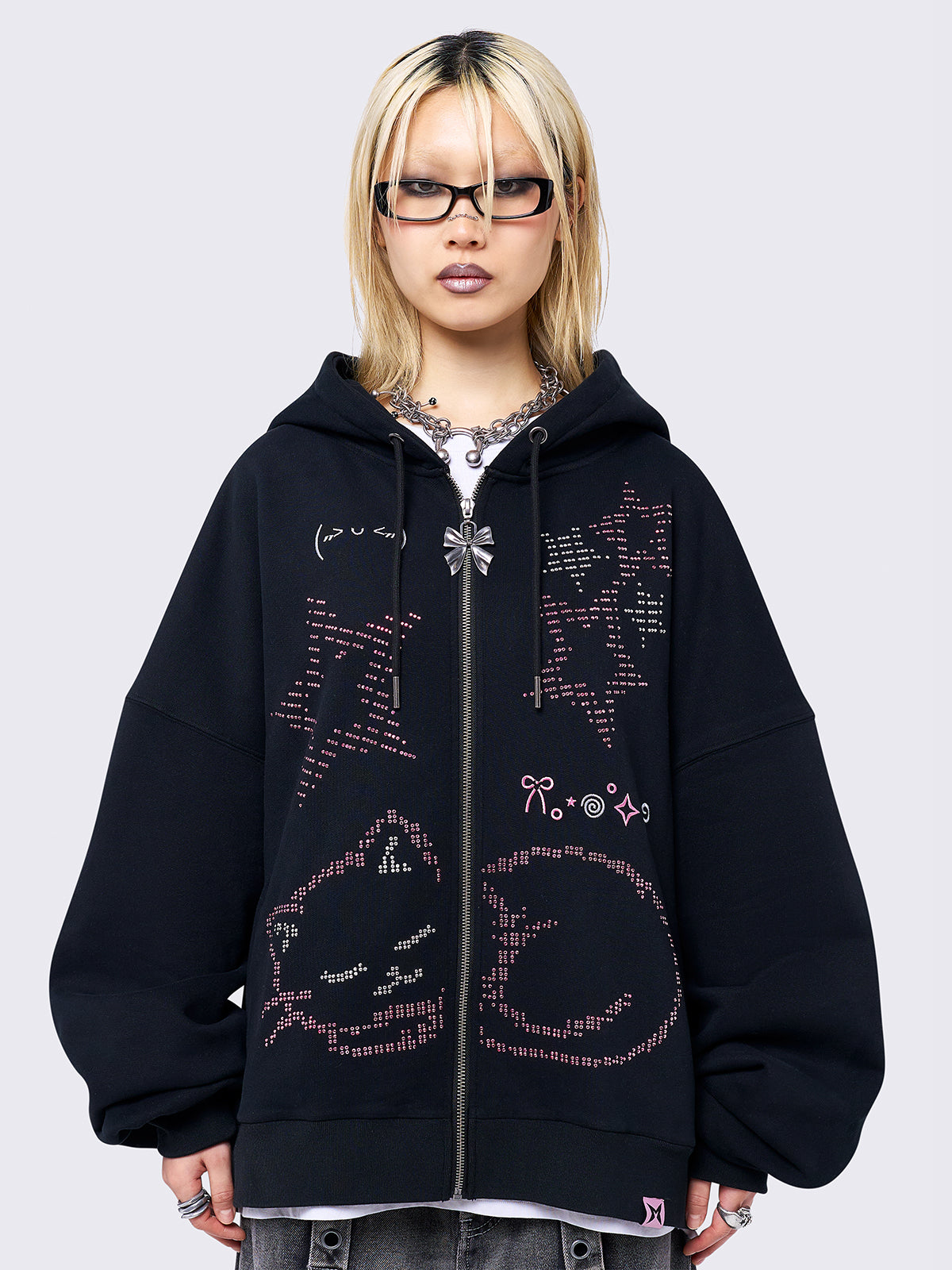 Black zip-up hoodie jacket featuring a pink cat and stars graphic with stud and embroidery details. Designed with a drawstring hood, zip fastening, long sleeves, ribbed trims, and an oversized fit.