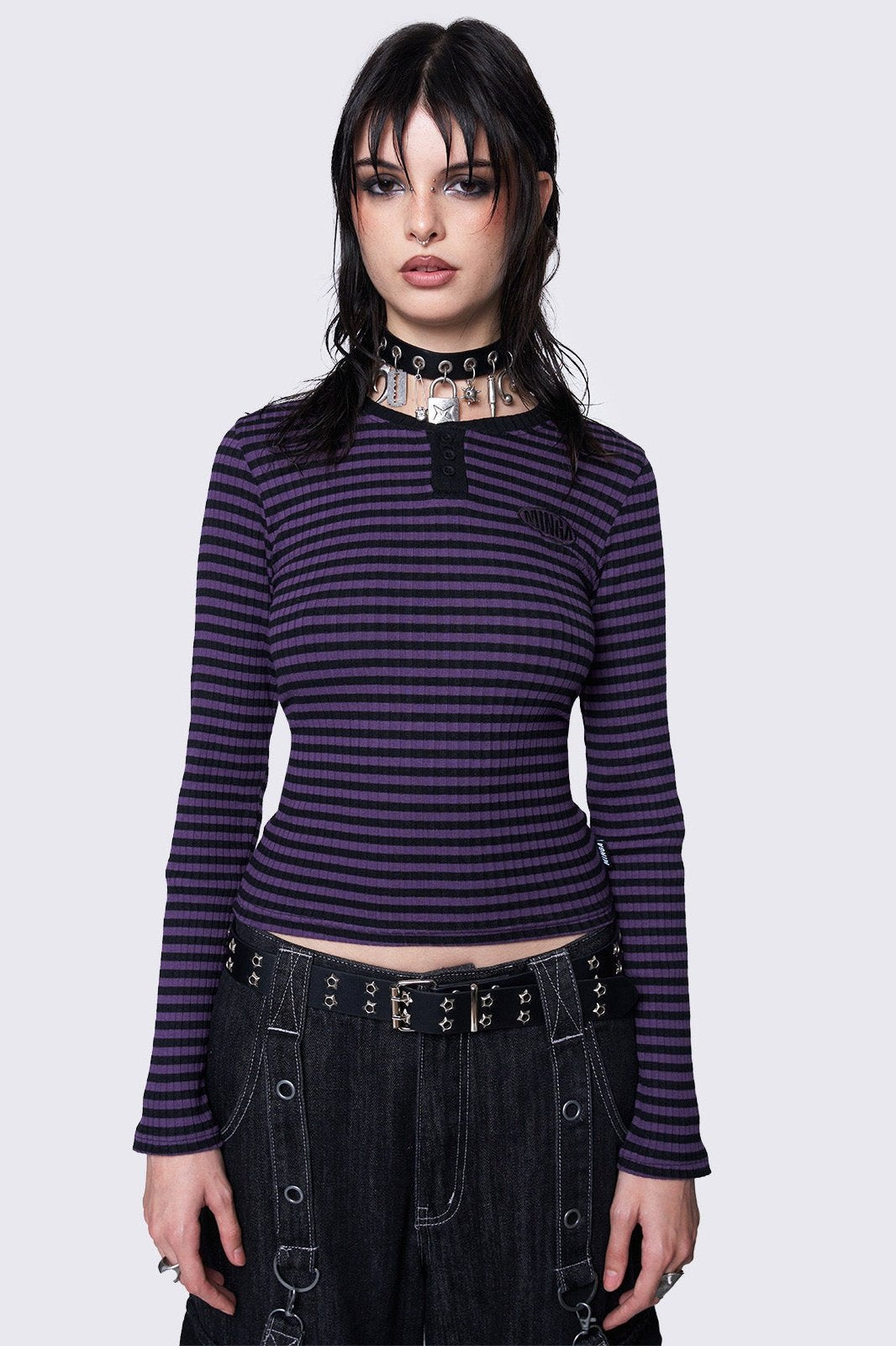 Slim-fit ribbed top with purple and black stripes, half button placket, Minga embroidered logo, and rounded neckline. Y2K and grunge-inspired style