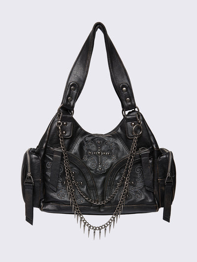 Black faux leather shoulder bag with silver chains, spike charms, side pockets, and embroidered cross detail on the front.