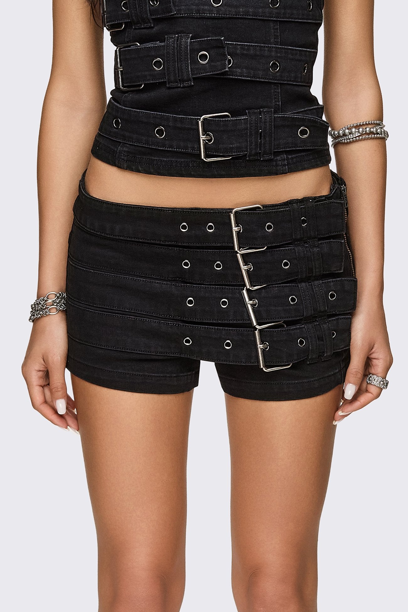 Black washed denim micro shorts with layered buckle straps and low-rise fit in a grunge goth style.