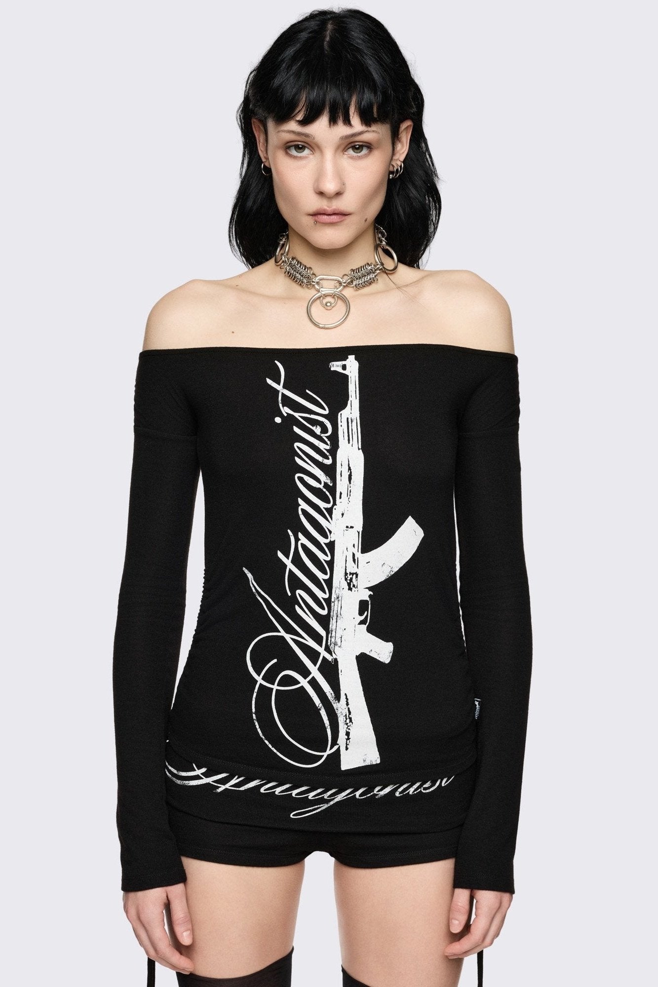 Black long sleeve off-shoulder top with "Antagonist" gun graphic front print and ruched tie side