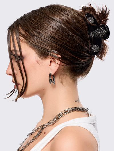 Black hair claw clip with silver floral baroque-style details.