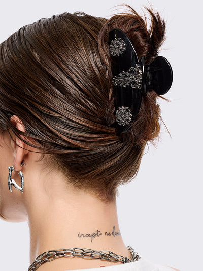 Black hair claw clip with silver floral baroque-style details.