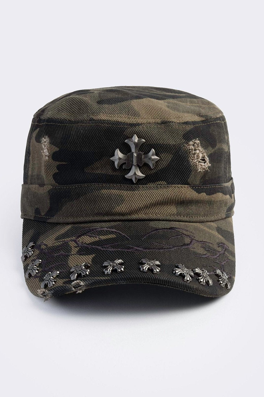flat-top military cadet cap in a green and brown forest camouflage print, featuring a large silver gothic cross emblem on the front and heavy distressed rips.