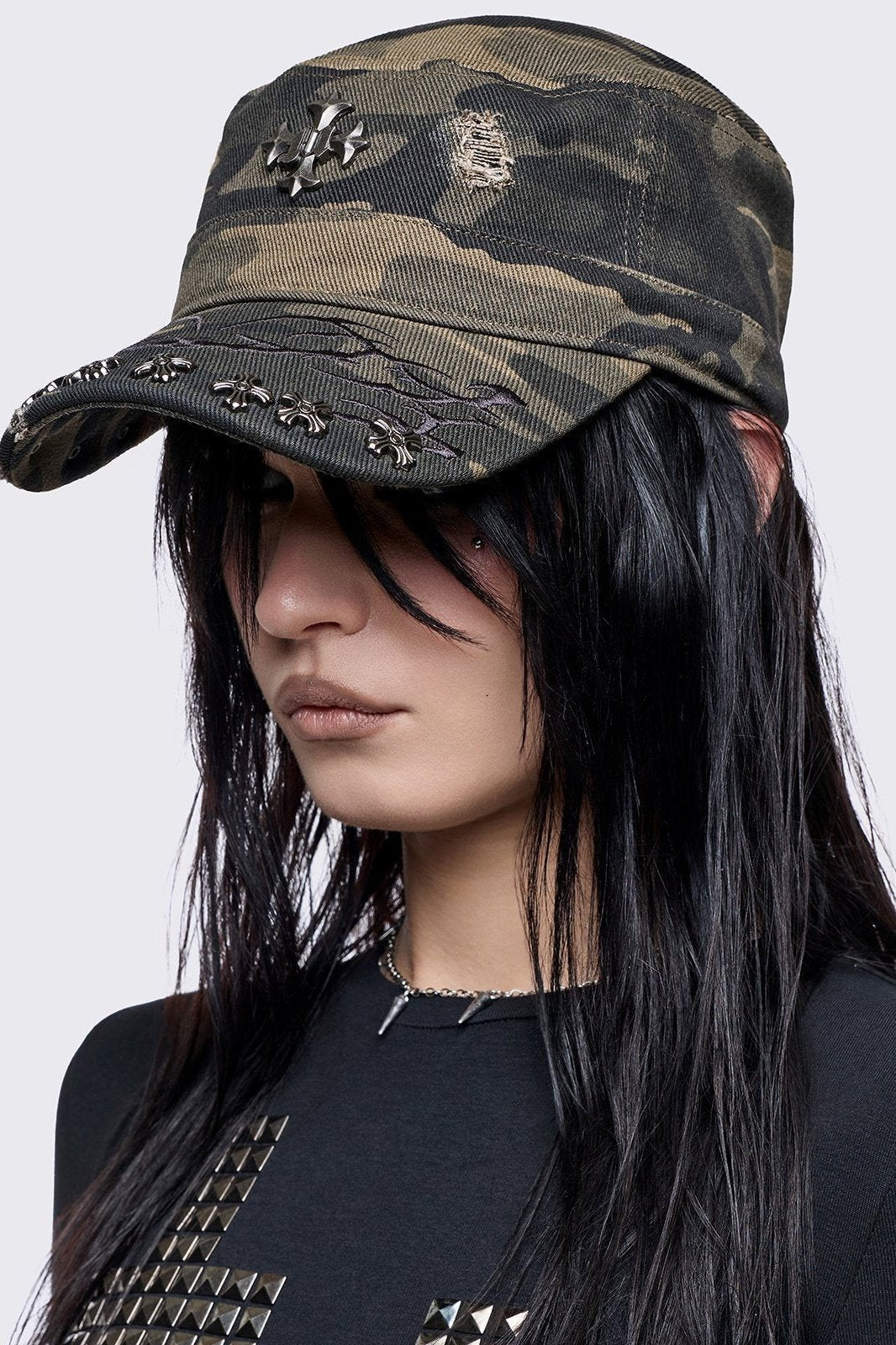 flat-top military cadet cap in a green and brown forest camouflage print, featuring a large silver gothic cross emblem on the front and heavy distressed rips.