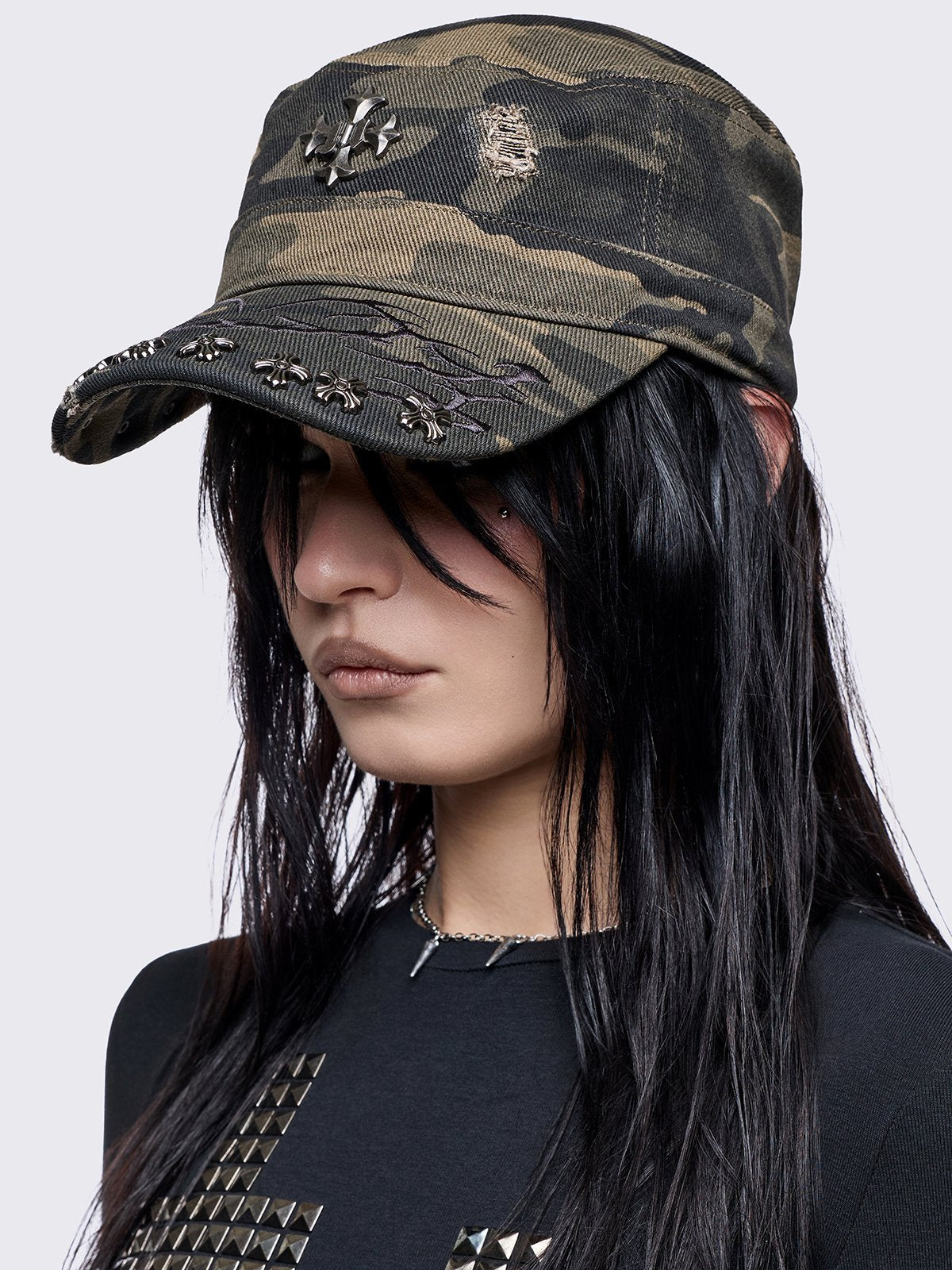 flat-top military cadet cap in a green and brown forest camouflage print, featuring a large silver gothic cross emblem on the front and heavy distressed rips.