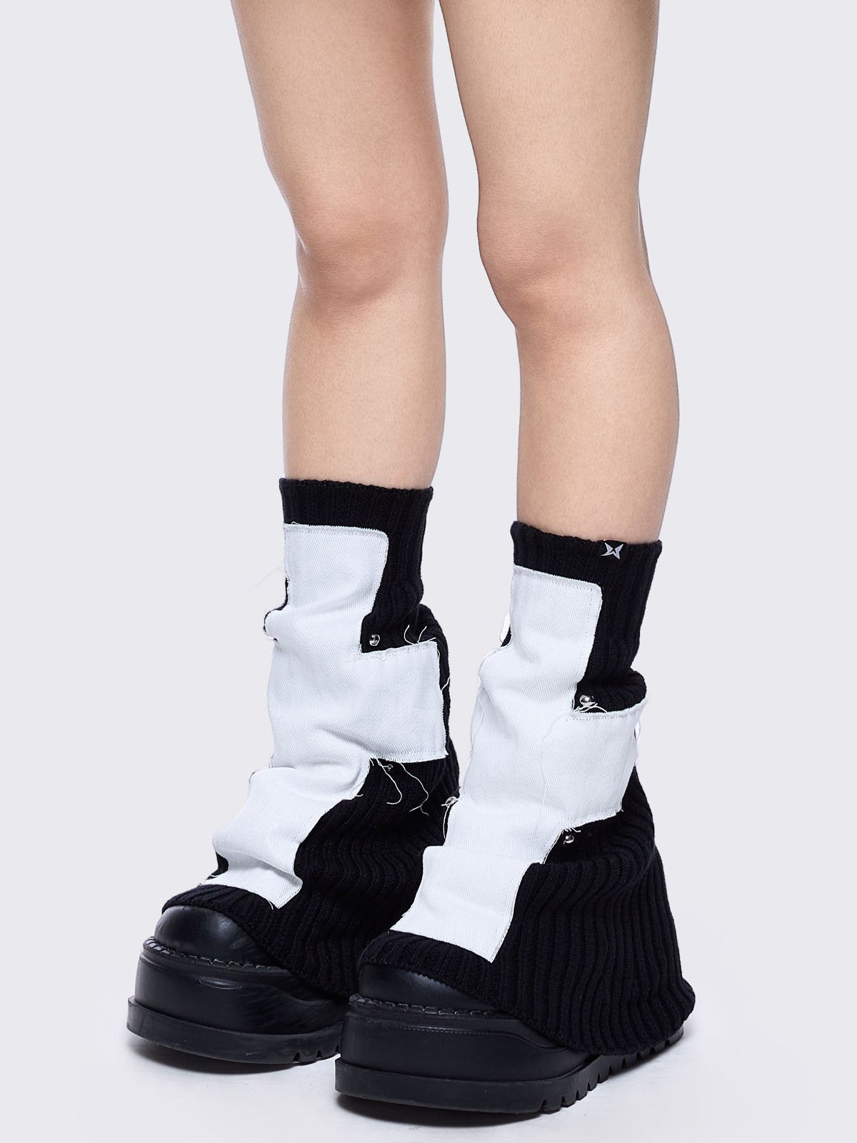 Black knitted flare leg warmers featuring a white chunky cross patch 