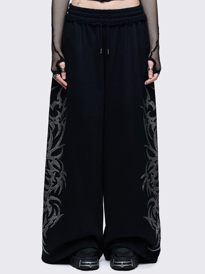Loose-fit wide-leg sweatpants featuring a large, detailed tribal sigil pattern made of silver rhinestones running down the side seam.