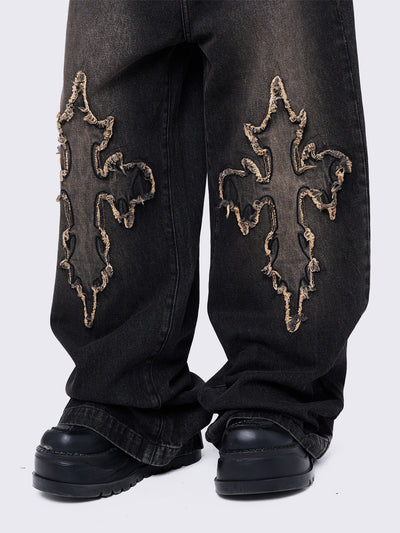 Black washed baggy jeans with brown overdye featuring a cross raw edge patches.