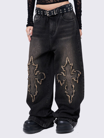 Black washed baggy jeans with brown overdye featuring a cross raw edge patches.