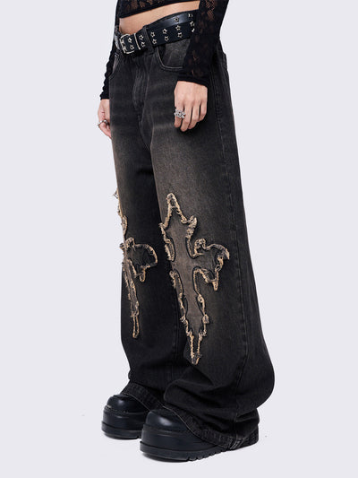 Black washed baggy jeans with brown overdye featuring a cross raw edge patches.