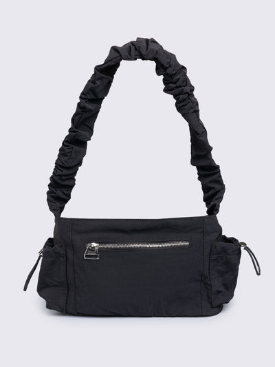 Black shoulder bag with ruched strap, lace-up ribbon front pockets, detachable plush pink bunny charm, and multiple pockets.