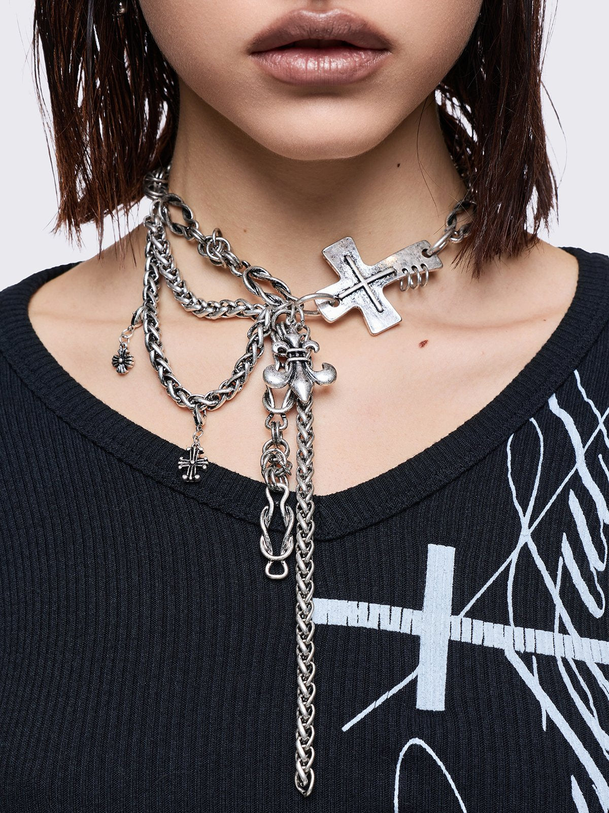 Layered necklace with chunky cross, fleur-de-lis and chain pendants.