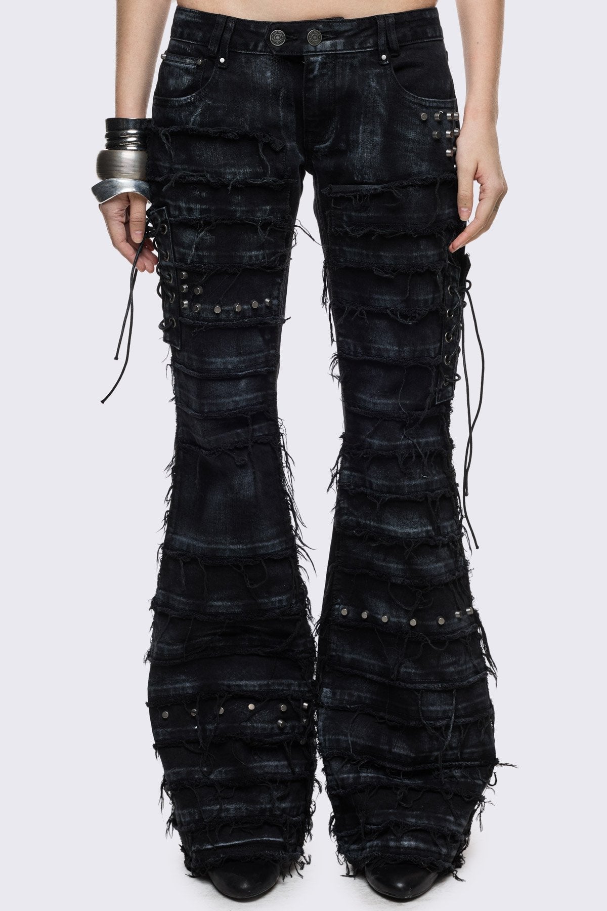 Black washed denim flare jeans with distressed panels, stud and lace-up details in a grunge Y2K style.