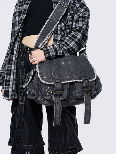 Black wash denim shoulder bag with frayed edges, flap closure, buckle straps, and studded details. Perfect for grunge and Y2K-inspired streetwear.