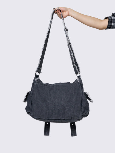 Black wash denim shoulder bag with frayed edges, flap closure, buckle straps, and studded details. Perfect for grunge and Y2K-inspired streetwear.