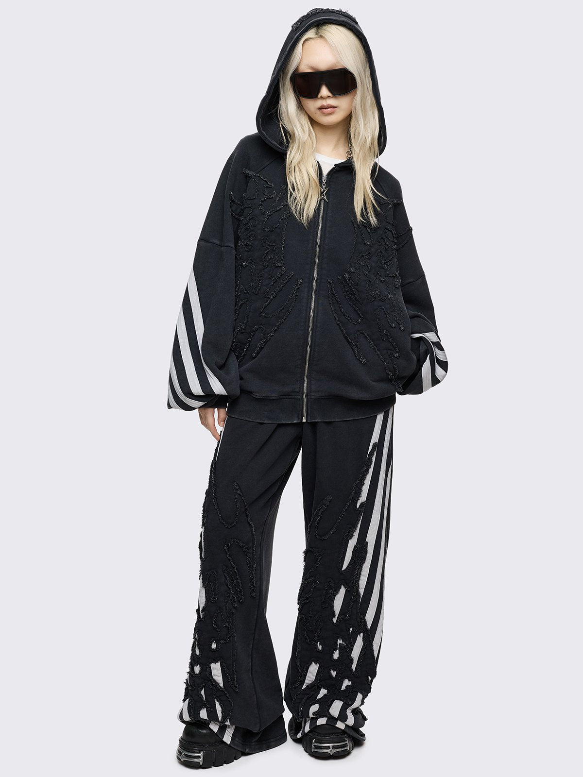 A pair of oversized black wide-leg sweatpants featuring white vertical side stripes and large, black flame-shaped overlays with raw, frayed edges.