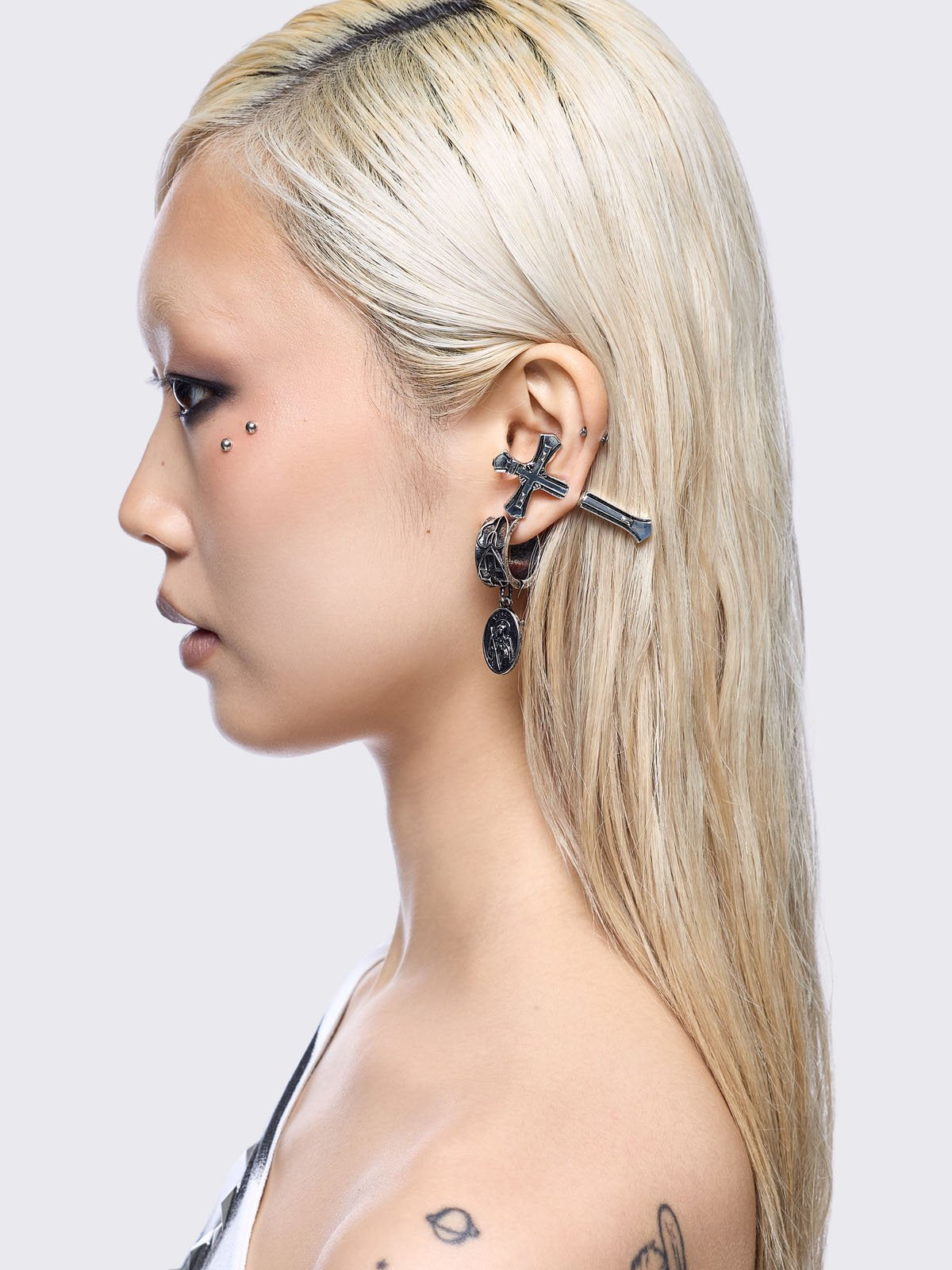 A 5-piece set of mismatched silver-toned earrings and an ear cuff featuring gothic and religious motifs, including crosses, a Virgin Mary medallion, and a winged sword dangle.