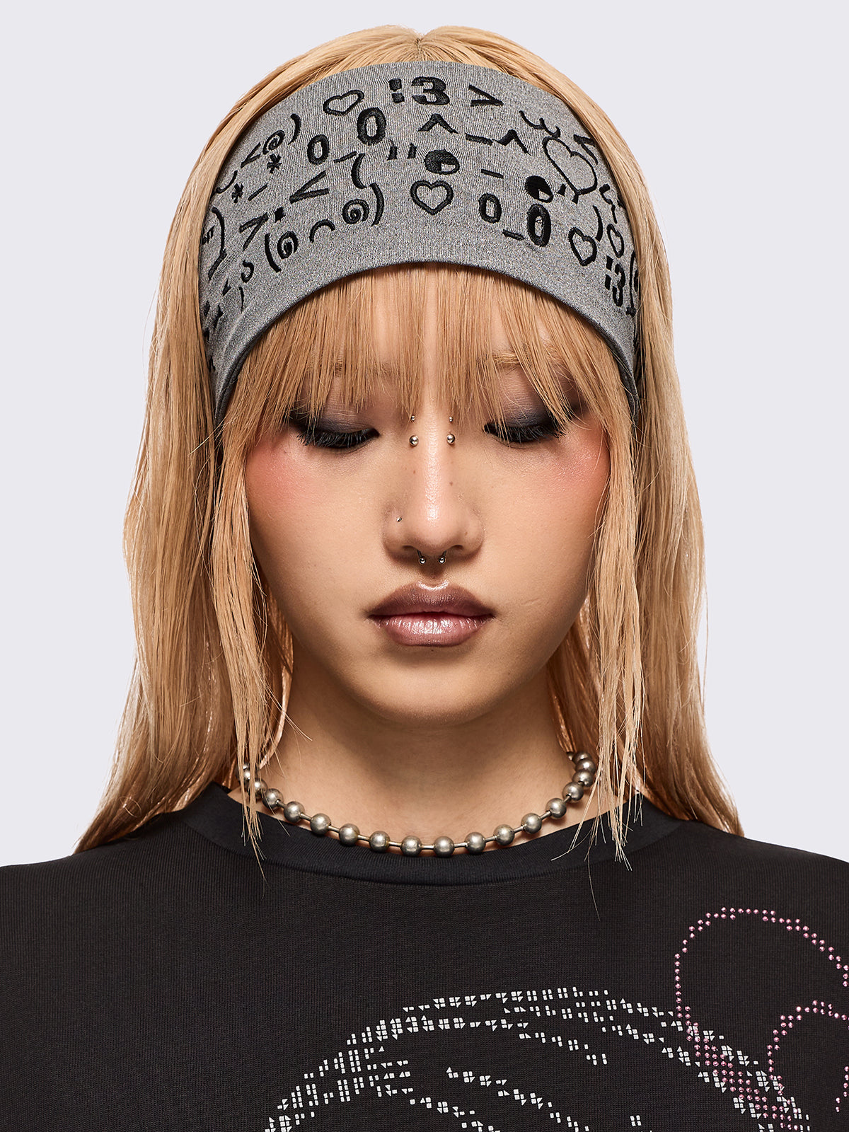 Grey wide headband with black kaomoji ASCII-style graphic embroidery.