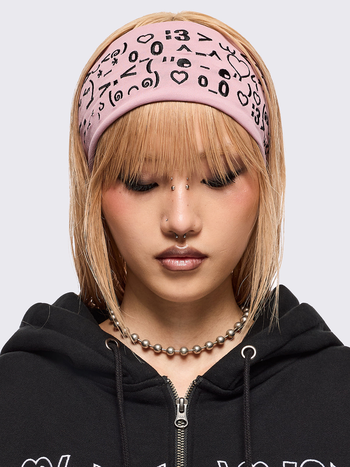 Pink wide headband with black kaomoji ASCII-style graphic embroidery.