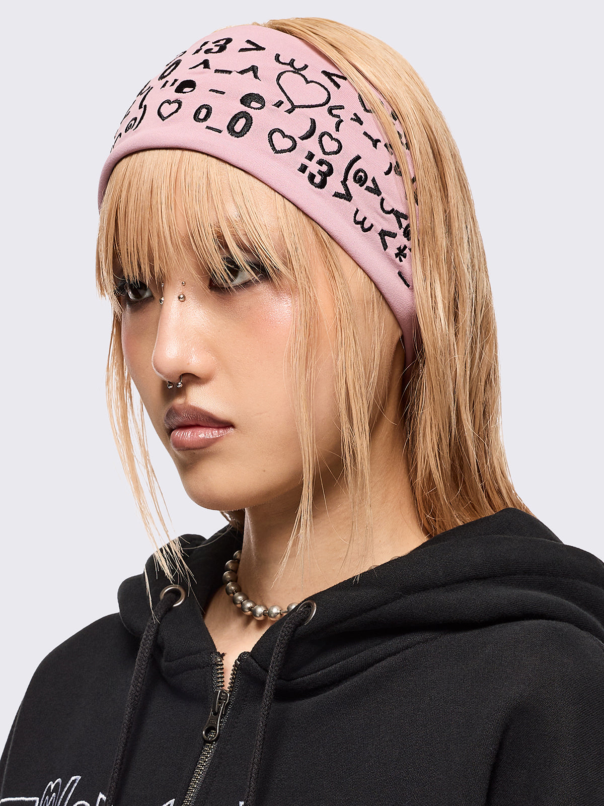 Pink wide headband with black kaomoji ASCII-style graphic embroidery.