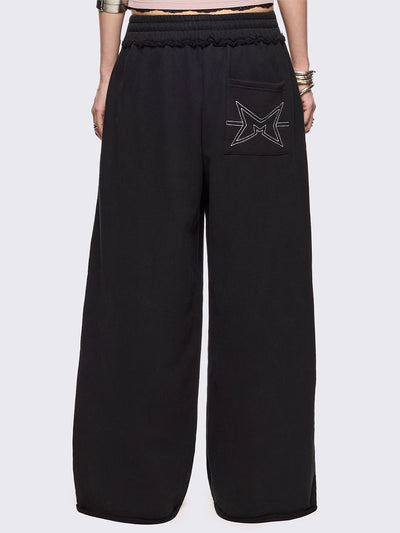 Black oversized sweatpants with all-over white emoticon and heart graphics in a playful ASCII/kaomoji style, styled in a relaxed streetwear fit.