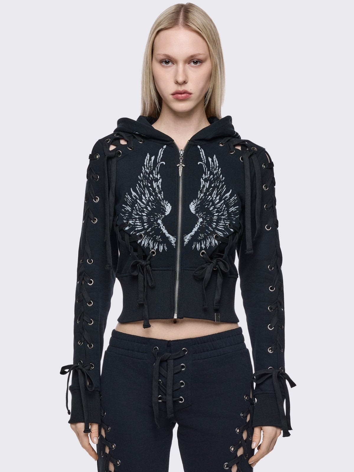 Black cropped zip up hoodie with open lace-up corset details down the sleeves and front and graphic print of wings on the front and hood