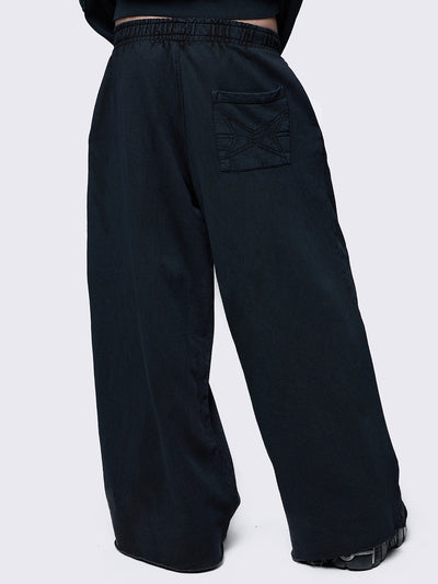 Wide-leg black joggers featuring adjustable buckle straps with grommet details, an elastic waistband, and an oversized fit. Designed for comfort and streetwear style.