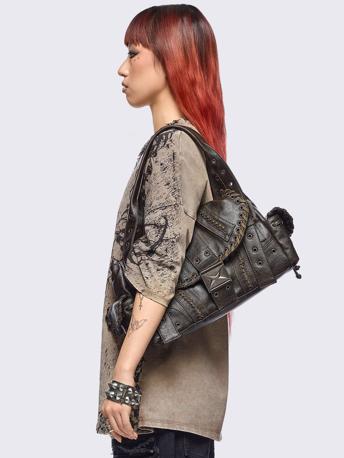 Brown faux leather shoulder bag featuring lace ups, eyelets, buckles and multiple pockets.