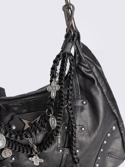 A black leather hobo bag decorated with silver studs, metallic charms, braided leather, and a large grey and white fur tail charm.