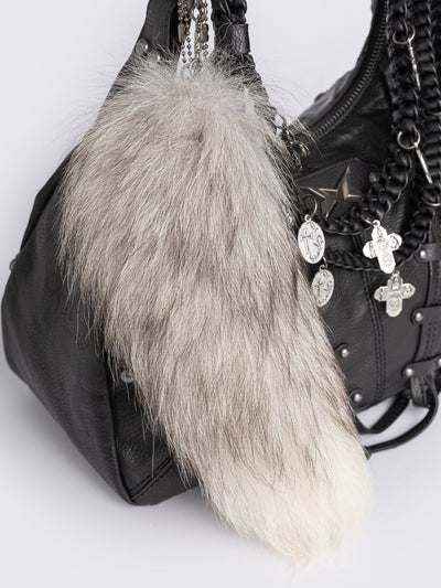 A black leather hobo bag decorated with silver studs, metallic charms, braided leather, and a large grey and white fur tail charm.