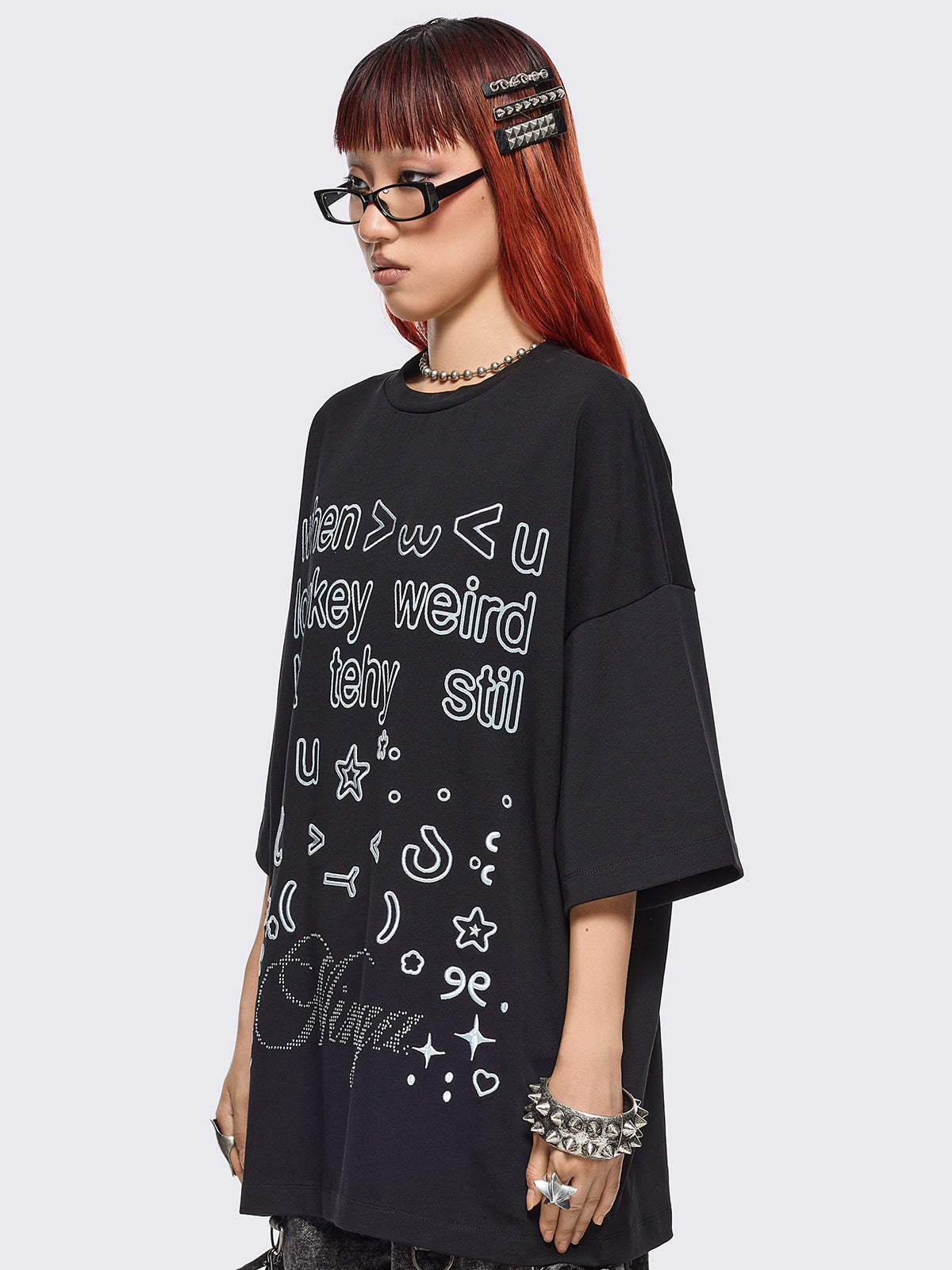 Black oversized t-shirt with "when u lowkey weird but tehy stil fw u" graphic print, kaomoji ASCII-style embroideries and stud details.