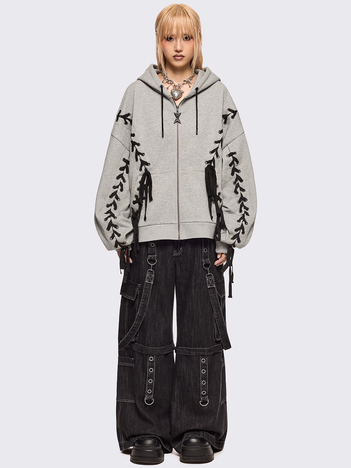 Grey marl zip-up hoodie with black lace corset details along the sleeves and front. Features a drawstring hood, zip fastening, long sleeves, and an oversized fit.