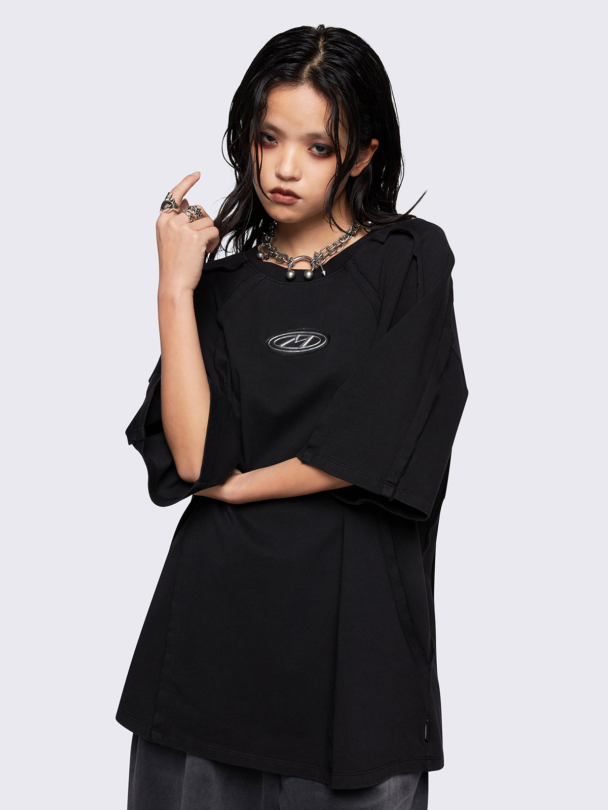 Black oversized t-shirt featuring exposed seams details and front metallic signature patch detail. 