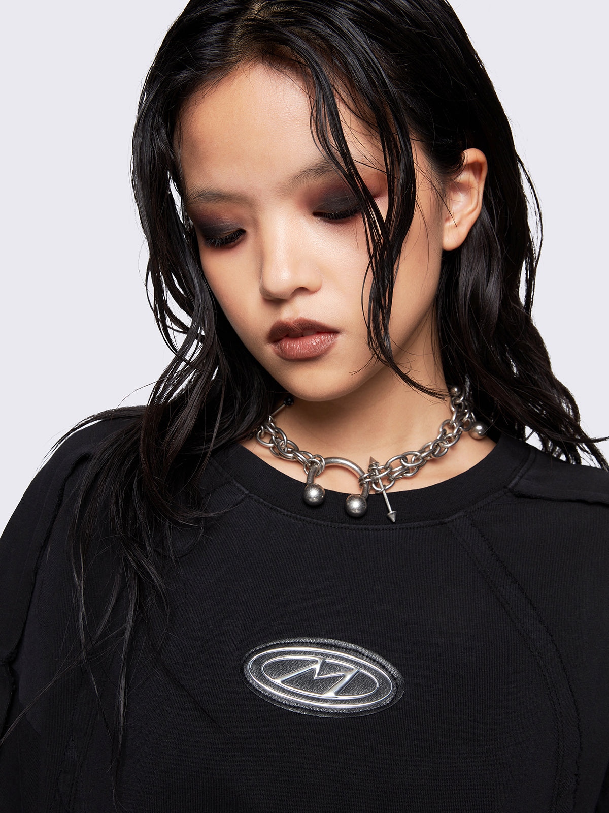 Black oversized t-shirt featuring exposed seams details and front metallic signature patch detail. 