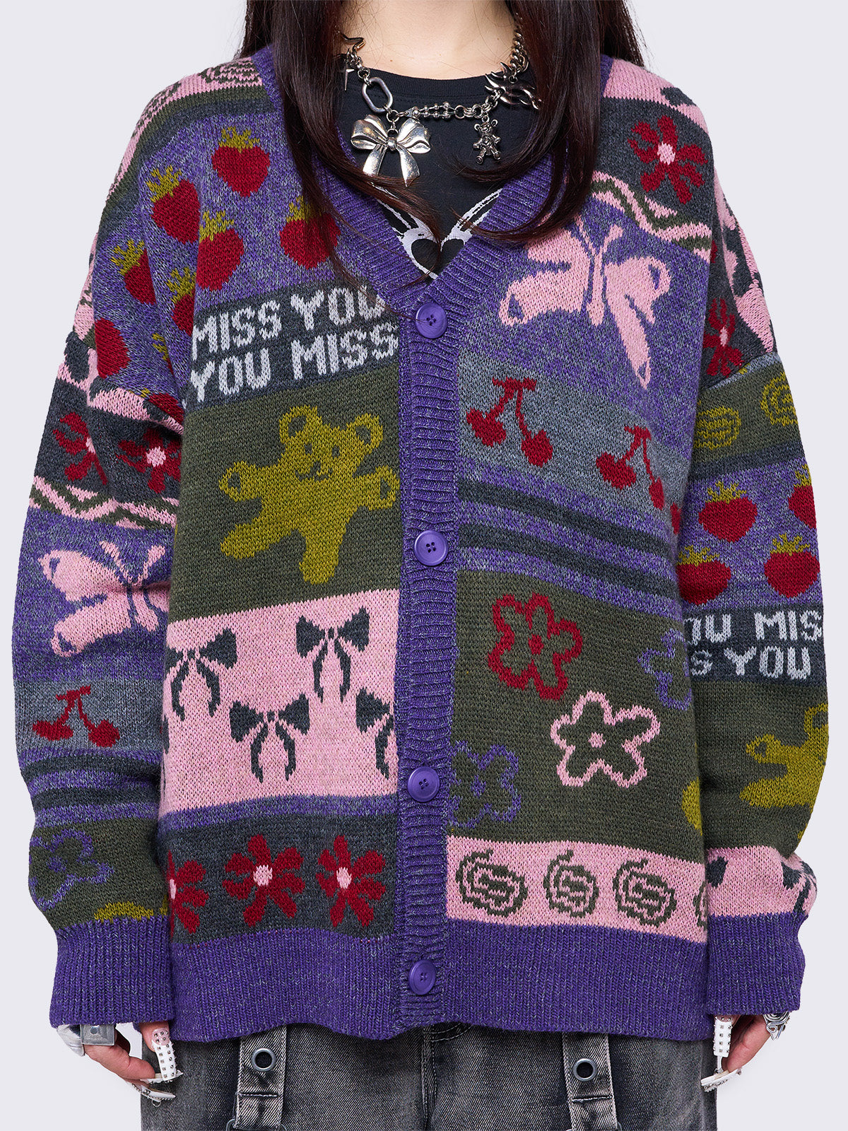 Purple jacquard knit cardigan with playful motifs including teddy bear, bows, flowers and geometric striped pattern.