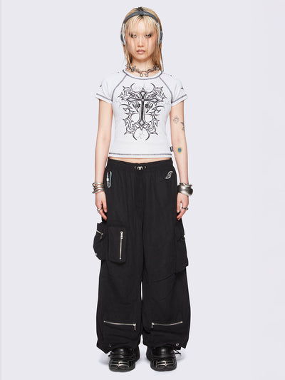 Black tech cargo parachute pants featuring multiple utility pockets with zipper and carabiner hardware detail - edgy, utility-inspired streetwear style.