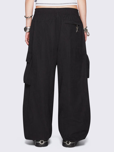 Black tech cargo parachute pants featuring multiple utility pockets with zipper and carabiner hardware detail - edgy, utility-inspired streetwear style.