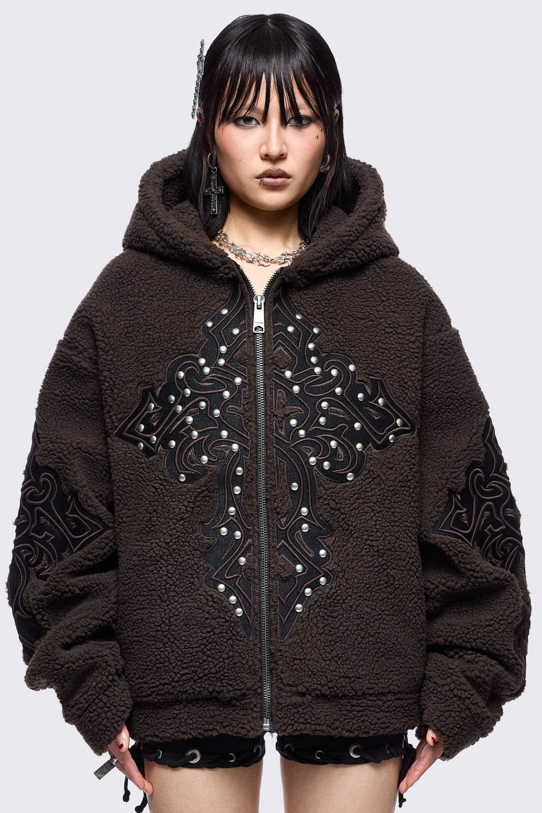 Brown fleece hoodie jacket featuring a cross patch on front and sleeves and silver stud details.