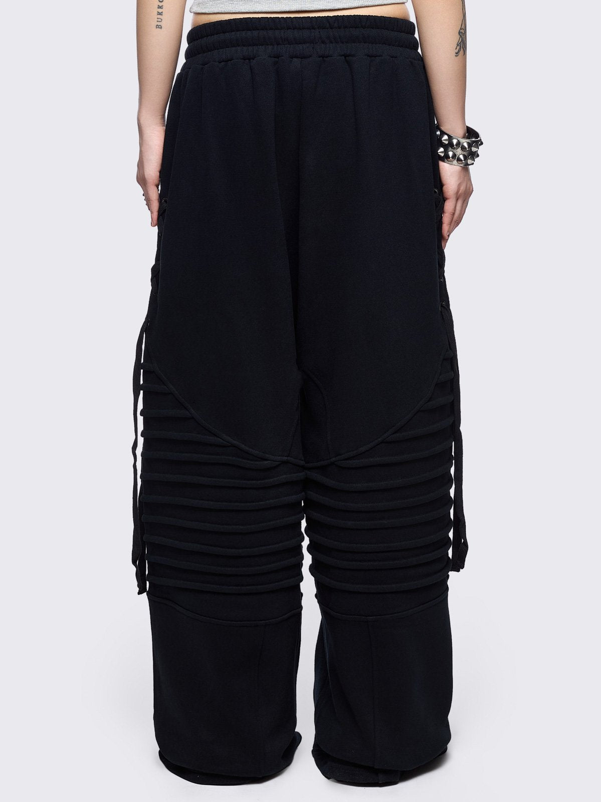 Black wide leg sweatpants featuring moto pintuck panels and lace-up details. 